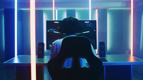 Back View Shot of the Professional Gamer Playing in First-Person Shooter Online Video Game on His P