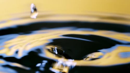 Close up real of water drop falls into water and diverging circles of water with smoot color backgro