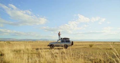Lone Traveler Stands Atop SUV in Grassy Expanse