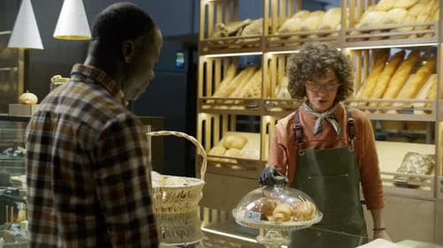 Female Sales Assistant Serving Fresh Pastries to Customer at Bakery Counter