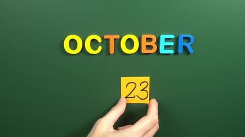 Hand sticking a sticker 23 October calendar day on school board. 23 date of October. Twenty third