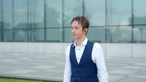 Focused Man Adjusting Earbud Walking Past Modern Building