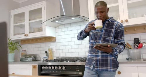 Young Man Drinks From Mug Using Tablet in Kitchen