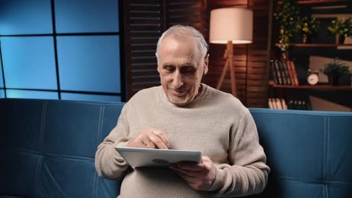 Man Using Tablet Sitting on Couch Indoors