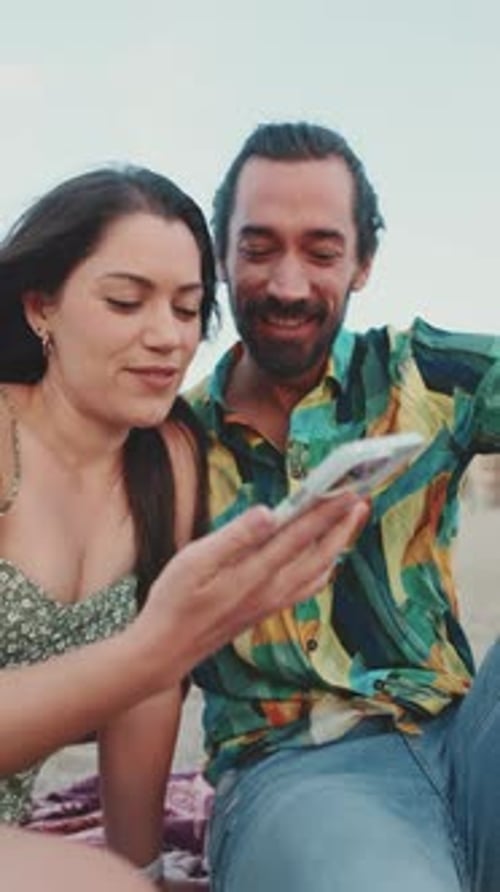 Romantic couple uses mobile phone while sitting on the beach