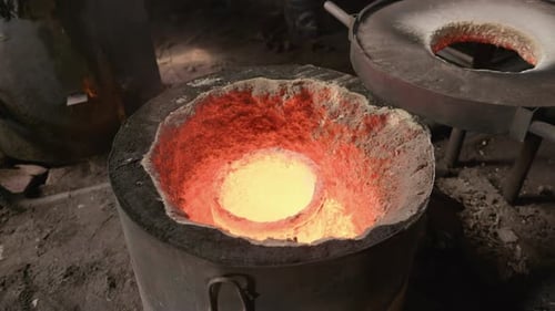 Wide slow motion smoldering open furnace with bright red melting pot in a rustic foundry factory