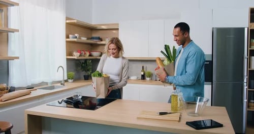 Multicultural couple takes fresh vegetables out of paper bag bought in supermarket. African American