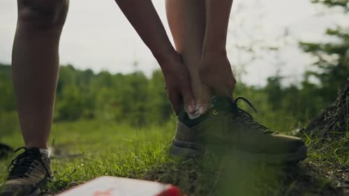 Woman Ties Hiking Shoe on Grassy Trail