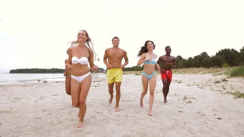 Happy multiethnic friends running joyfully on a sunny beach summer vacation