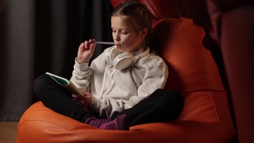 preteen school girl pupil with headphones on shoulders is taking notes, studying at home. Schoolchil