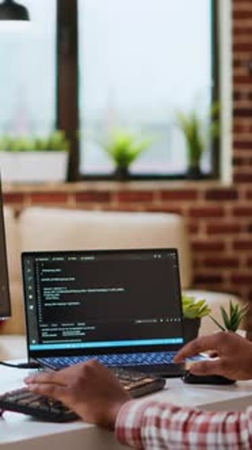 Vertical Video Young Man Seen Programming Software Code on His Laptop in a Sleek Home Office