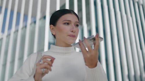 Stylish young businesswoman recording voice message on phone in modern city