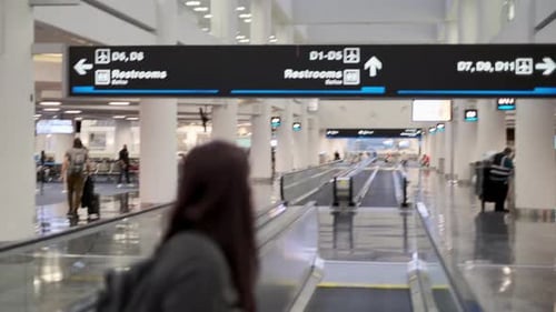 Tilt down from airport terminal sign to woman wearing a mask on a moving walkway.