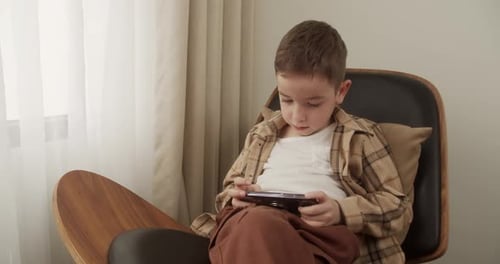 Boy Playing Game on Smartphone in Modern Chair