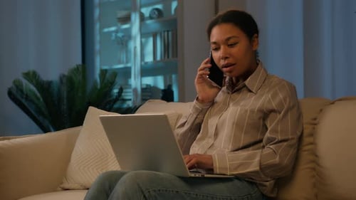 Woman Using Laptop and Phone on Sofa at Night