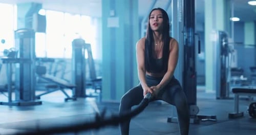 Fit Woman Using Battle Ropes in Gym