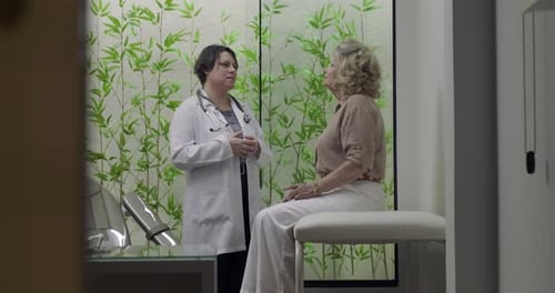 Doctor discussing medical condition with senior female patient sitting on exam table during clinic