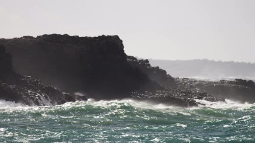 Olas tormentosas bañan las rocas mientras el sol brilla en la superficie del agua.