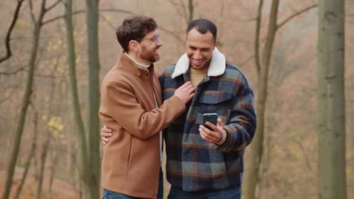Shot of Happy Hugging Homosexual Male Couple Looking at Photos on Smartphone
