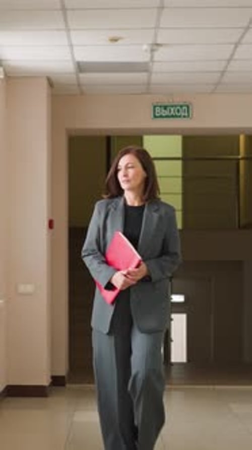 Businesswoman Walking Through Office Corridor Holding Folder and Coffee