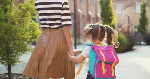 Rückansicht junge Frau hält kleines Mädchen im weißen Kleid von Hand, geht in die Stadt zur Schule, Studium