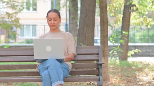 Woman Works on Laptop in Park on Bench