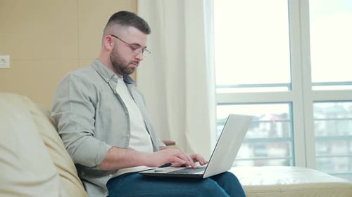 Man Typing on Laptop on Couch in Living Room