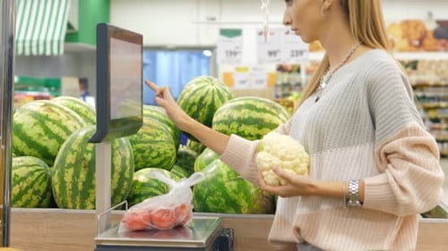 A Young Pretty Customer Weighs Groceries and Vegetables in a Supermarket in the Selfservice