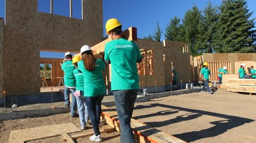 Volunteers Carry Lumber at House Construction Site on Sunny Day