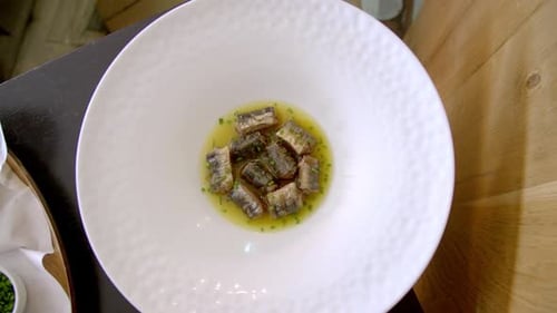 A gourmet dish of grilled fish pieces garnished with herbs in a white bowl, showcasing elegant prese
