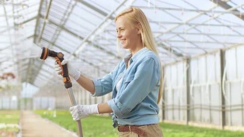 Smiling Woman Watering Flowers in Sunny Greenhouse