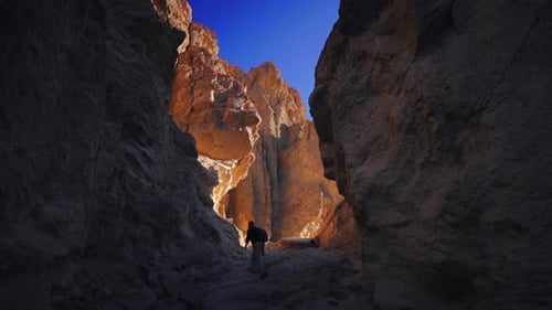 Wanderer, der durch den Dramatisch Wüsten-Canyon mit goldenen, sonnenbeschienenen Felswänden geht