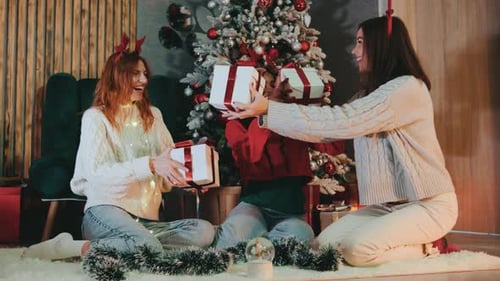 Women Exchanging Christmas Gifts in Front of Tree