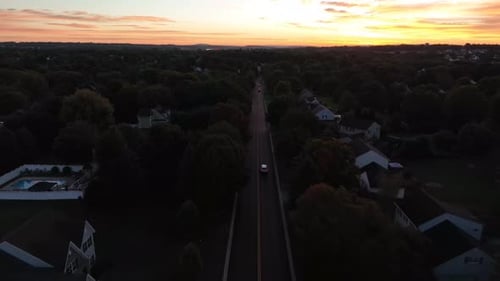 Imagen aérea inversa de automóviles que viajan por una tranquila carretera que atraviesa un vecindario en Estados Unidos.