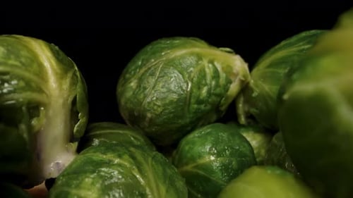 A pile of cooked Brussels sprouts, as the camera moves backward through them and a woman adds a coup