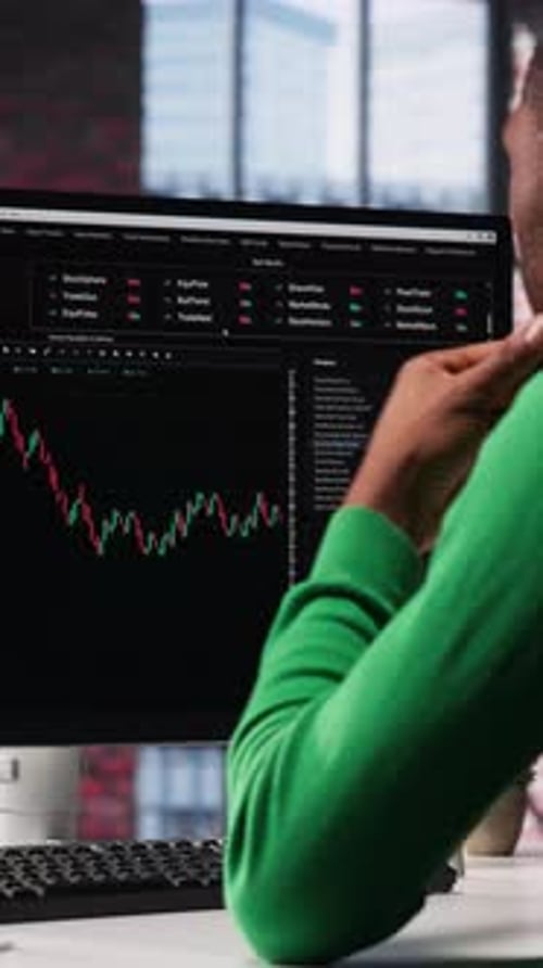 Adult Reviews Financial Data at Computer Workstation