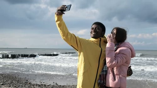 Happy couple taking selfie at beach on cloudy day