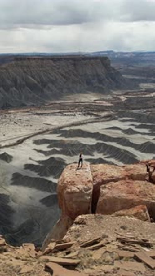 Vertical Drone Shot of Woman Standing on The Edge of Cliff Above Abyss and Desert Landscape
