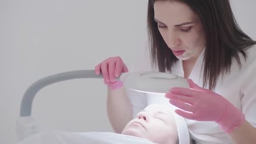 Beautician Uses Magnifying Lamp to Examine Client's Skin and Cure Skin Problems During Spa Facial