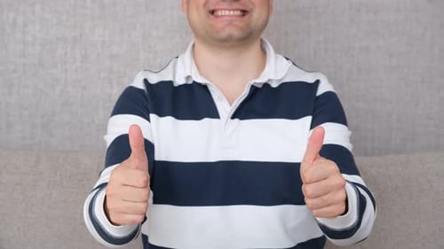 Man Gives Thumbs Up on Gray Couch