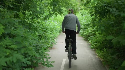 Young Boy Riding Bicycle Through Green Tunnel on Paved Pathway