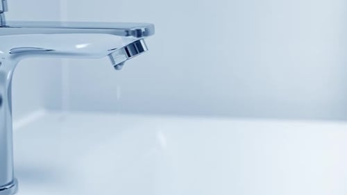 Water Drops From Silver Faucet in White Sink