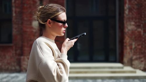 Female Recording Voice Message on Mobile Phone While Walking Down Street