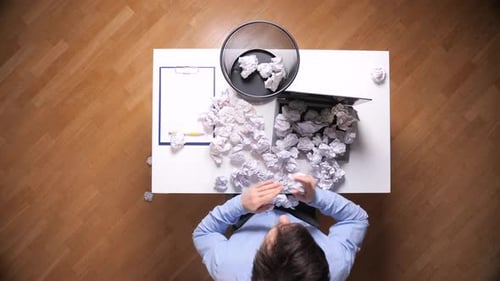 Man Tossing Crumpled Paper Into Trash Can At Desk