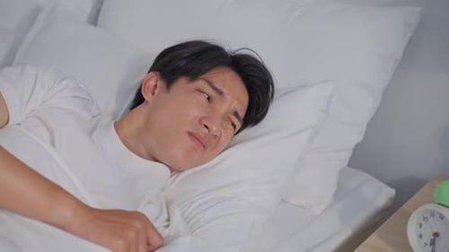 Asian attractive young man turn off alarm clock ringing in the morning.