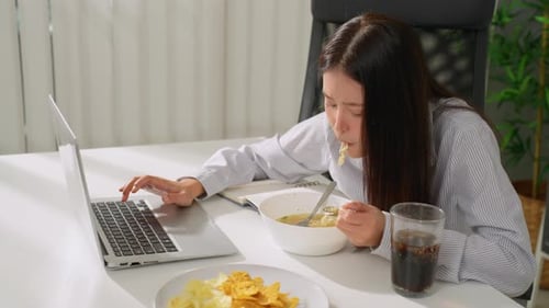 Asian young businesswoman eating noodles while working in the office.