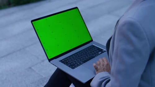 Person Scrolling on Laptop with Green Screen Outdoors