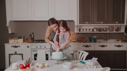 Mom teaches her daughter to cook a cake by squeezing out the cream. Mommy kisses her daughter.
