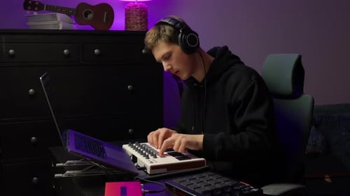 Young man composing music on midi keyboard at home
