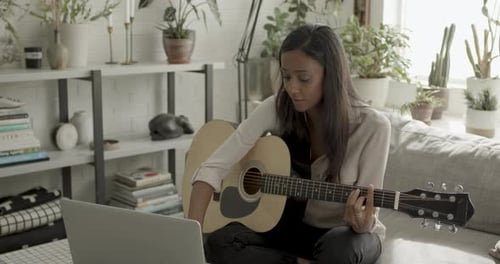 Woman Playing Acoustic Guitar while Looking at Laptop
